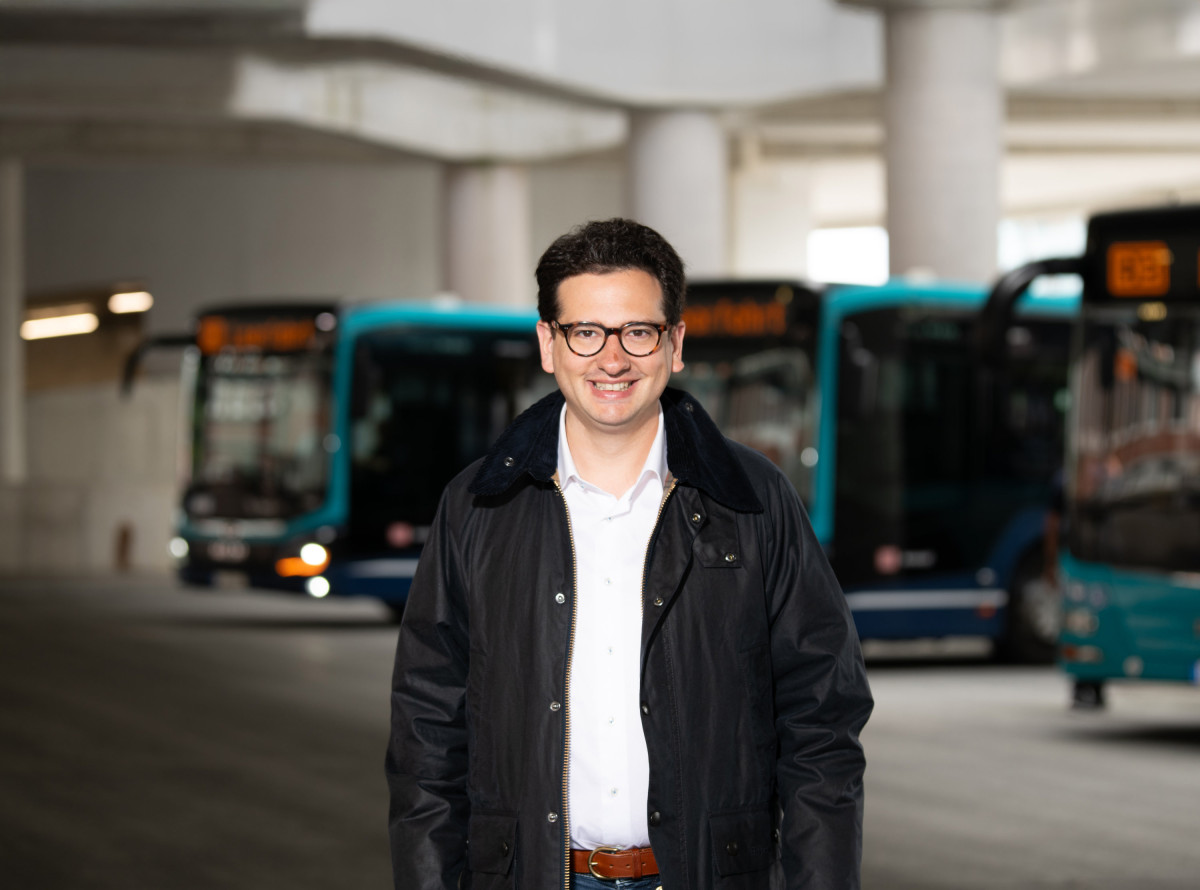 Bastian Mahmoodi steht in einem Depot mit Linienbussen. Er blickt zentral in die Kamera.