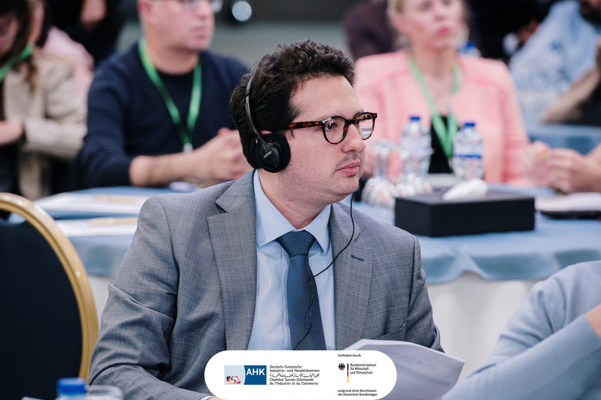 Bastian Mahmoodi hört mit Kopfhörern einer Konferenz der Deutsch-Tunesischen Industrie- und Handelskammer zu.