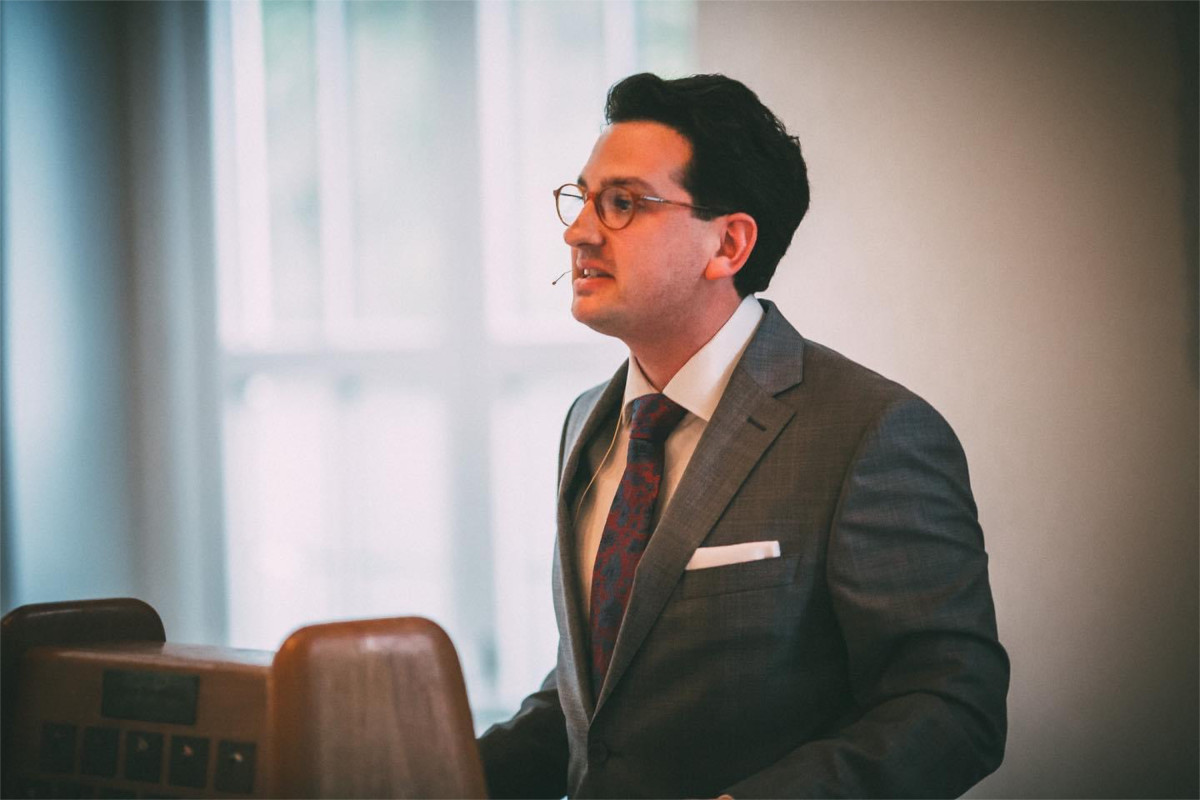 Bastian Mahmoodi spricht mit Headset-Mikrofon während einer Veranstaltung in einem hellen Raum.