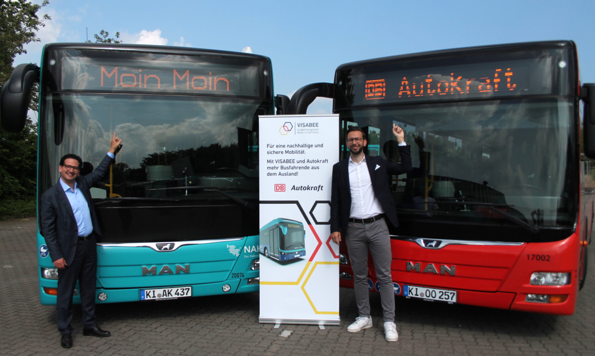 Bastian Mahmoodi und ein Kollege stehen vor zwei Bussen mit den Schriftzügen „Moin Moin“ und „DB Autokraft“ sowie einem VISABEE-Banner.